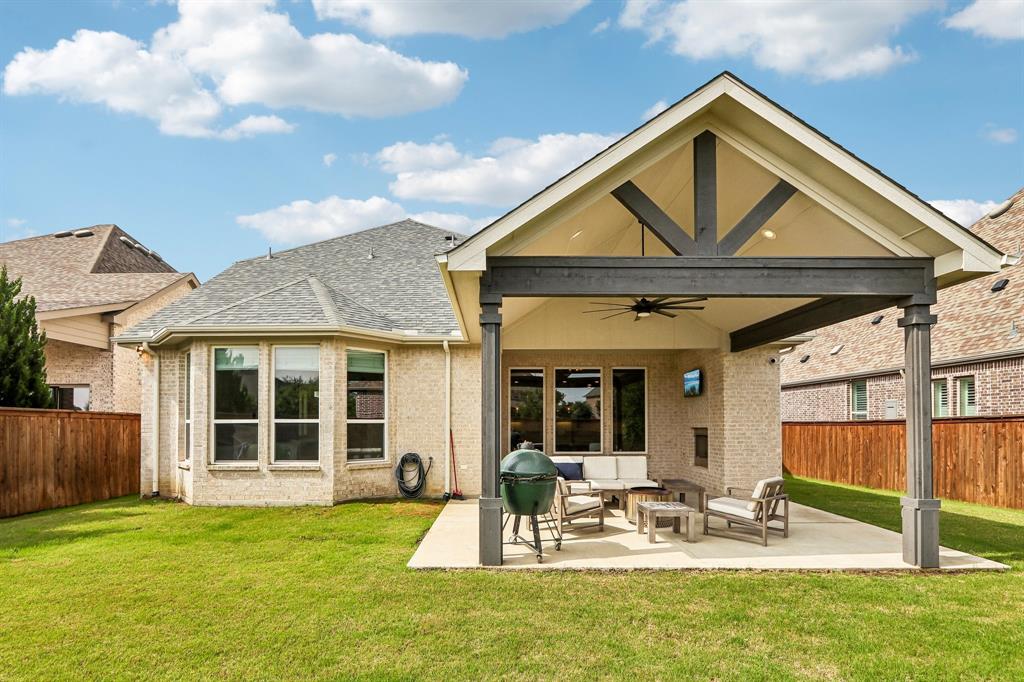 Expansive backyard featuring a covered patio, vaulted ceiling with exposed beams, ceiling fan, and brick fireplace