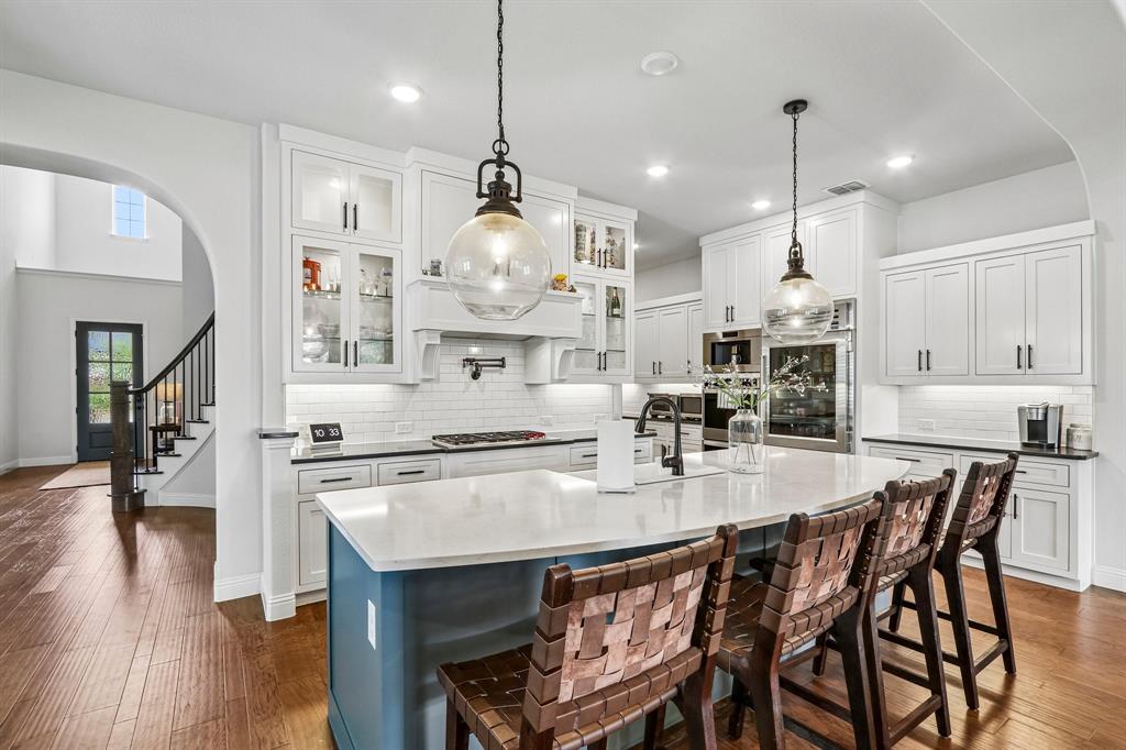 Gourmet kitchen with white cabinetry, a large center island with seating, built-in stainless steel appliances, and wood-finish flooring Gourmet kitchen with white cabinetry, a large center island with seating, built-in stainless steel appliances, and wood-finish flooring
