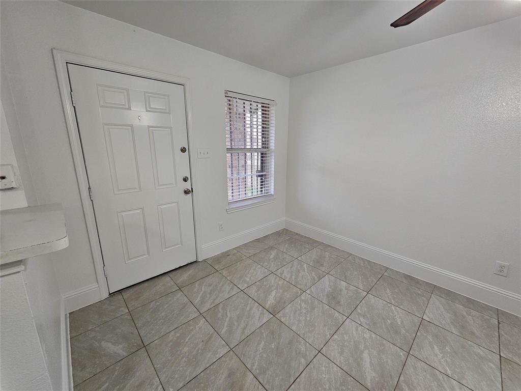 White paneled door, window with blinds, wood-finish ceiling fan, neutral tile flooring, and white baseboards