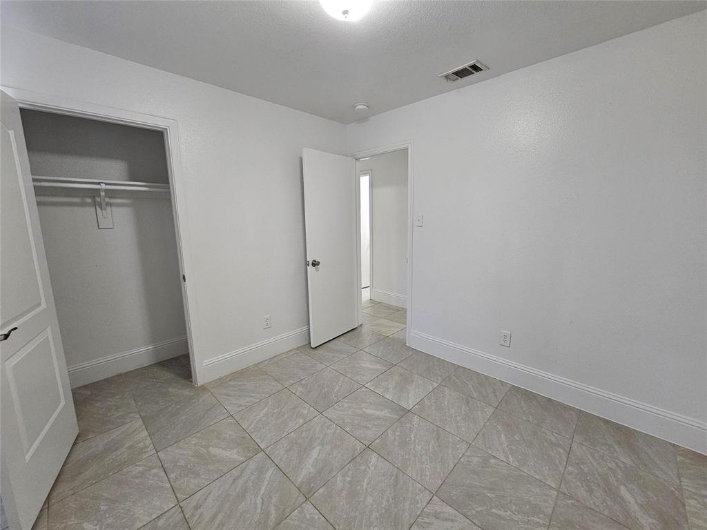 Square tile flooring, white walls, recessed ceiling light, and a built-in closet with hanging rod