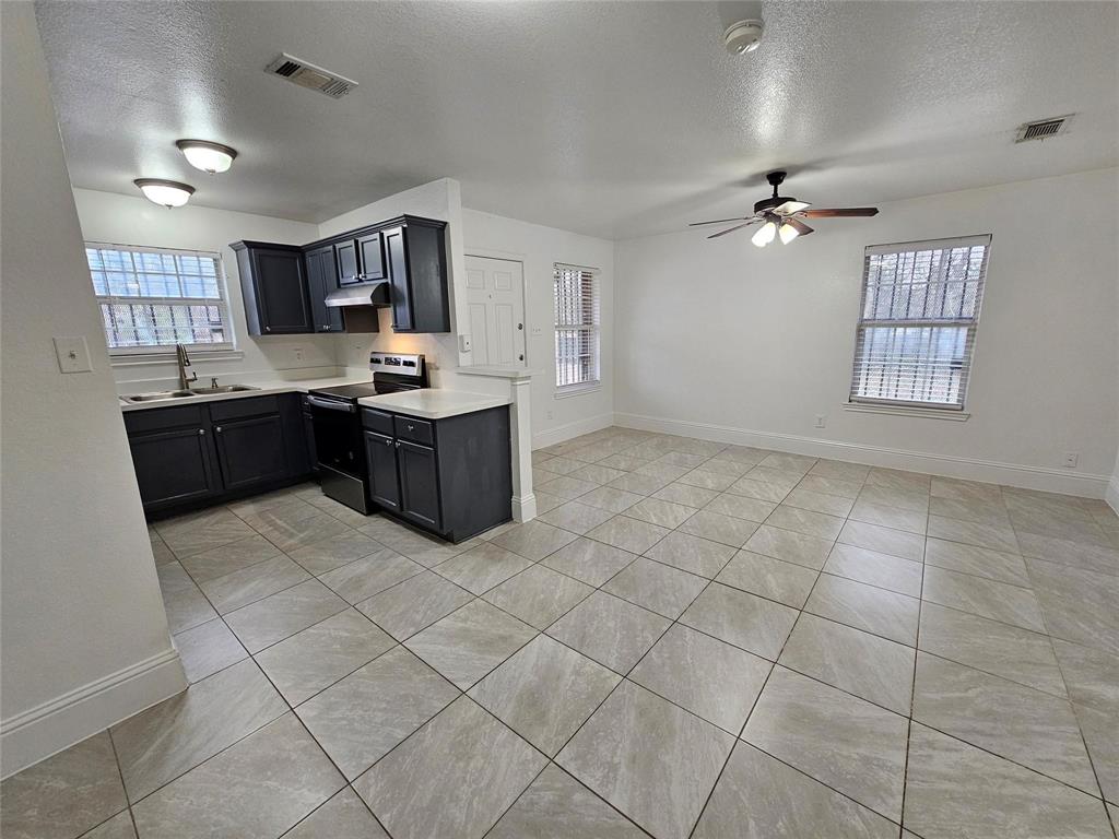 Open-concept living space with tile flooring, dark cabinetry, light countertops, and a ceiling fan
