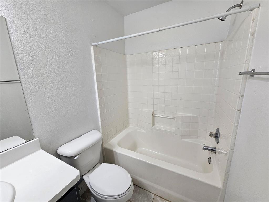 White tiled shower/tub combination with a built-in shelf, adjacent toilet, and vanity with a countertop
