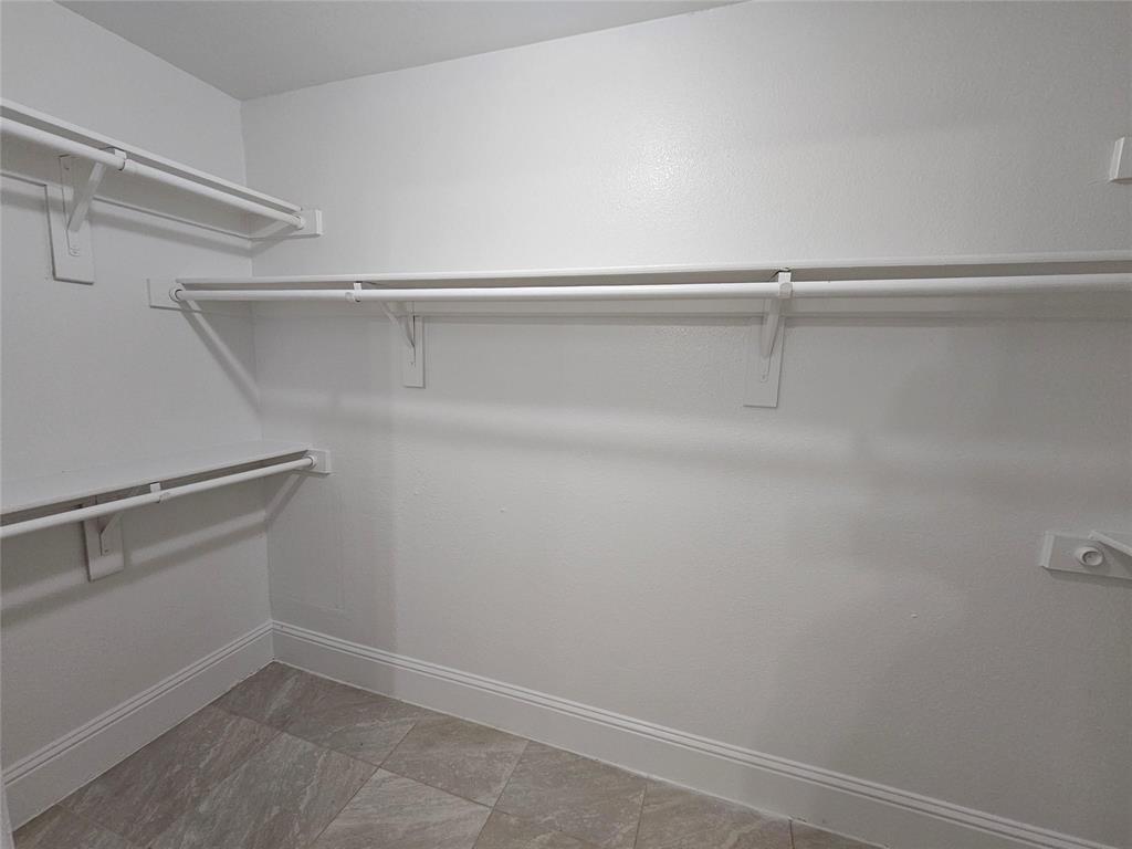 Walk-in closet with multiple white shelving units and hanging rods, complemented by light-toned tile flooring and white trim