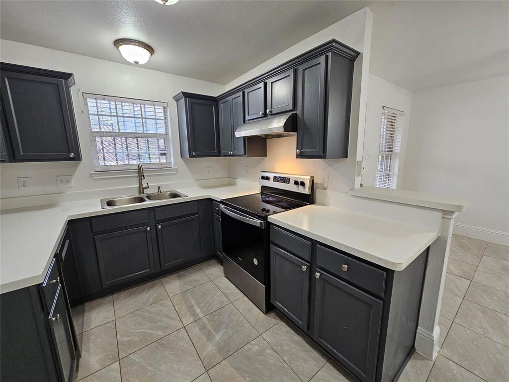 Modern kitchen featuring dark cabinetry, stainless steel sink, contemporary faucet, stainless steel electric range, and tile flooring