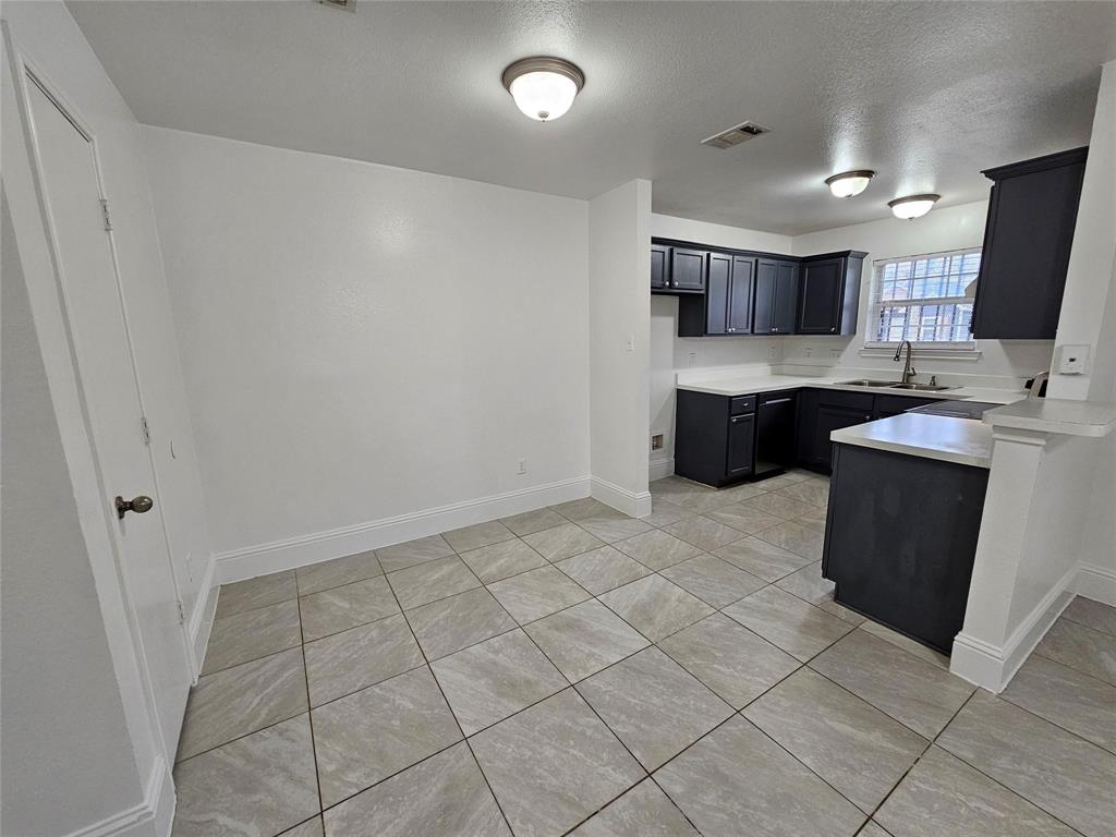 Kitchen and dining area featuring tile flooring, dark cabinetry, light countertops, and a stainless steel sink
