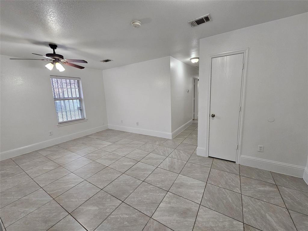 Spacious room featuring neutral tile flooring, window with horizontal blinds, and a ceiling fan with integrated lighting