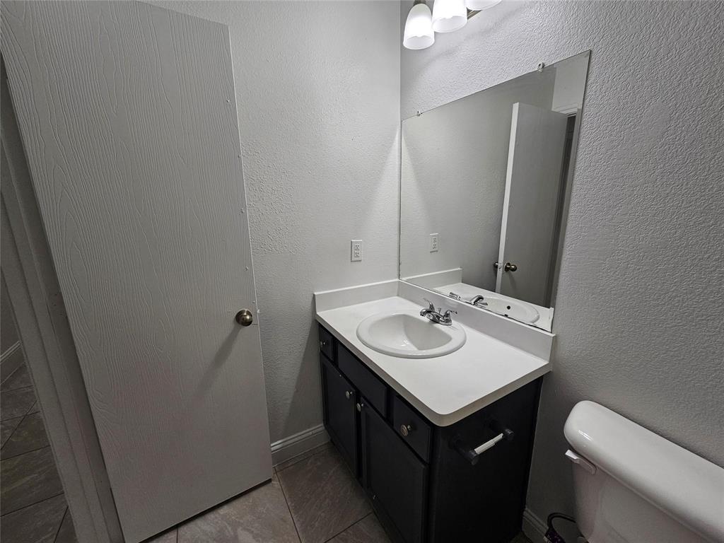 Vanity with a white countertop and integrated sink, chrome faucet, wall-mounted mirror, and tile flooring