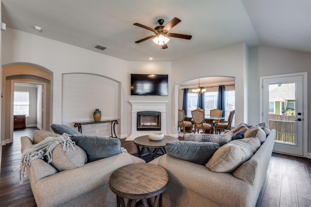 Vaulted ceiling with a ceiling fan, fireplace with a white mantel, arched doorways, wood-finish flooring, and a glass-paneled exterior door