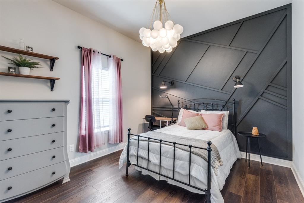 Accent wall with geometric molding, wood-finish flooring, built-in wall sconces, ceiling-mounted light fixture, and window with blinds