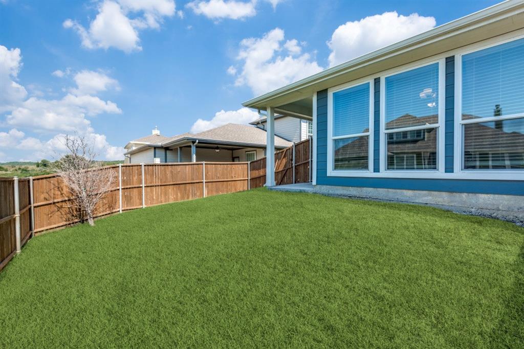 Spacious backyard featuring a wood privacy fence, covered patio, and multiple large windows
