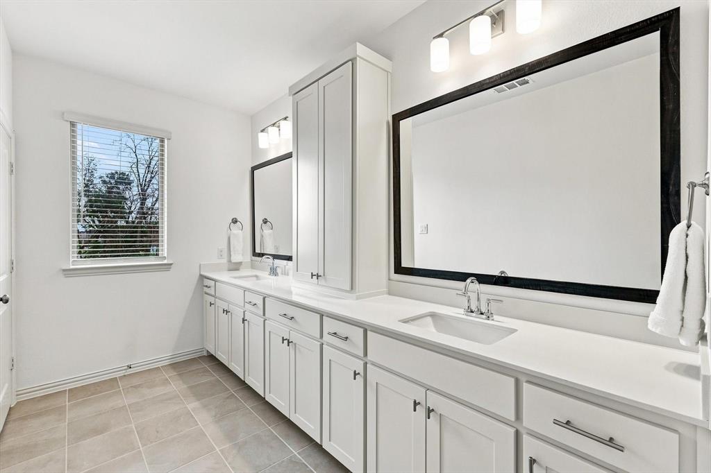 Bright and beautifully appointed, the primary bath offers dual sinks, extensive counter space, generous storage, and natural light.