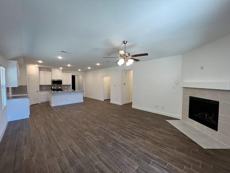 Open-concept living area with wood-finish flooring, a tiled fireplace, and recessed lighting