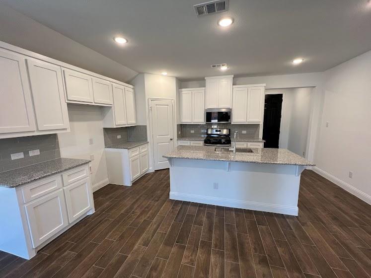 Open-concept kitchen featuring white cabinetry, light-toned countertops, a central island with an integrated sink, modern stainless steel appliances, and wood-finish flooring