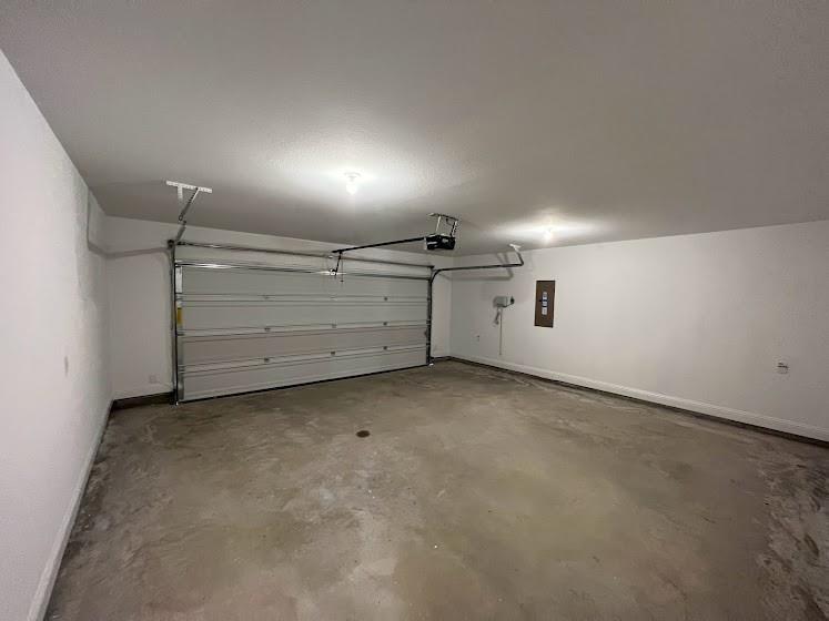 Enclosed garage with a white sectional door, exposed overhead door mechanism, concrete flooring, and ceiling-mounted lighting