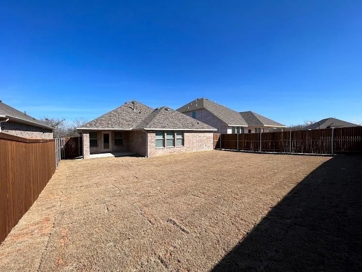 Expansive backyard with a full privacy fence, brick exterior, and covered patio