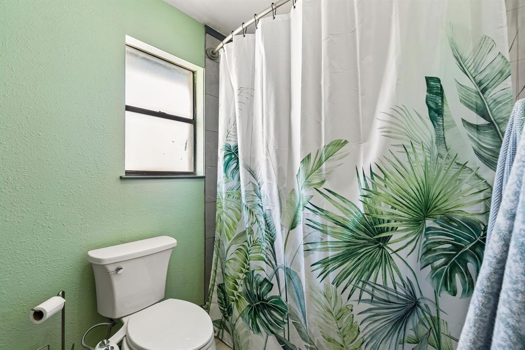 Compact bathroom with a two-piece toilet, tiled shower surround, and a window for natural light