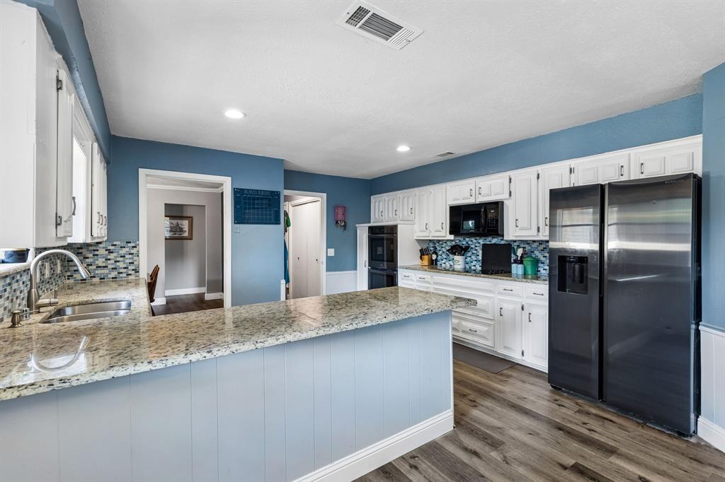 Kitchen featuring wood-finish flooring, white cabinetry, granite countertops, and a mosaic tile backsplash