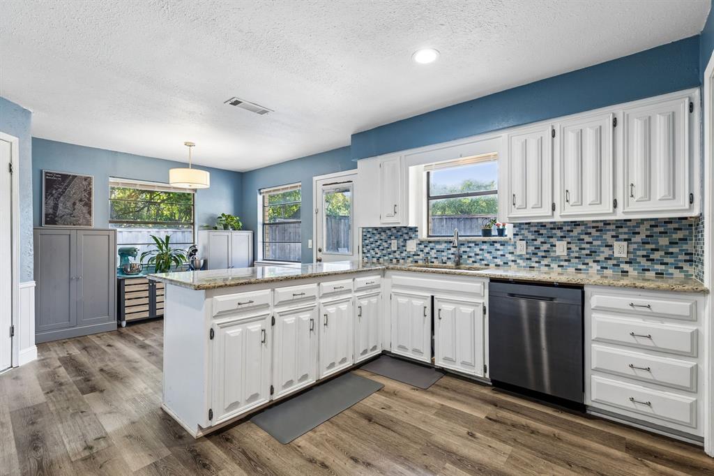 Modern kitchen featuring white cabinetry, stainless steel appliances, geometric tile backsplash, wood-finish flooring, and abundant natural light from multiple windows and glass doors overlooking the outdoor space