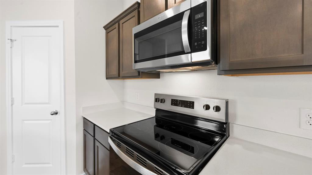 Stainless steel microwave, dark wood-finish cabinetry, light-toned countertops, and a white paneled door
