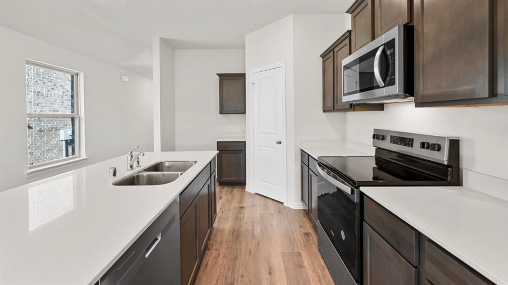 Modern kitchen featuring wood-finish flooring, dark wood cabinetry, white countertops, and stainless steel appliances Modern kitchen featuring wood-finish flooring, dark wood cabinetry, white countertops, and stainless steel appliances
