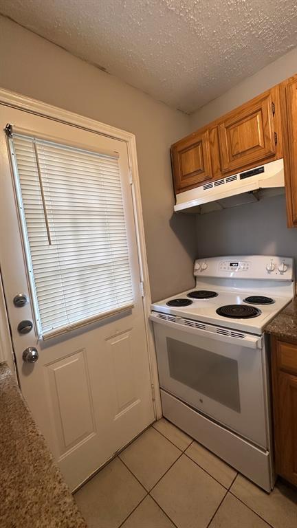 White electric range, wood cabinetry, and tile flooring