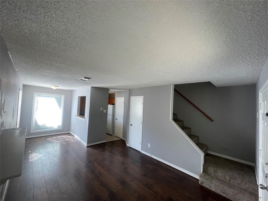 Open-concept interior featuring wood-finish flooring, a pass-through window to the kitchen, a staircase with a wooden handrail, and carpeted stairs