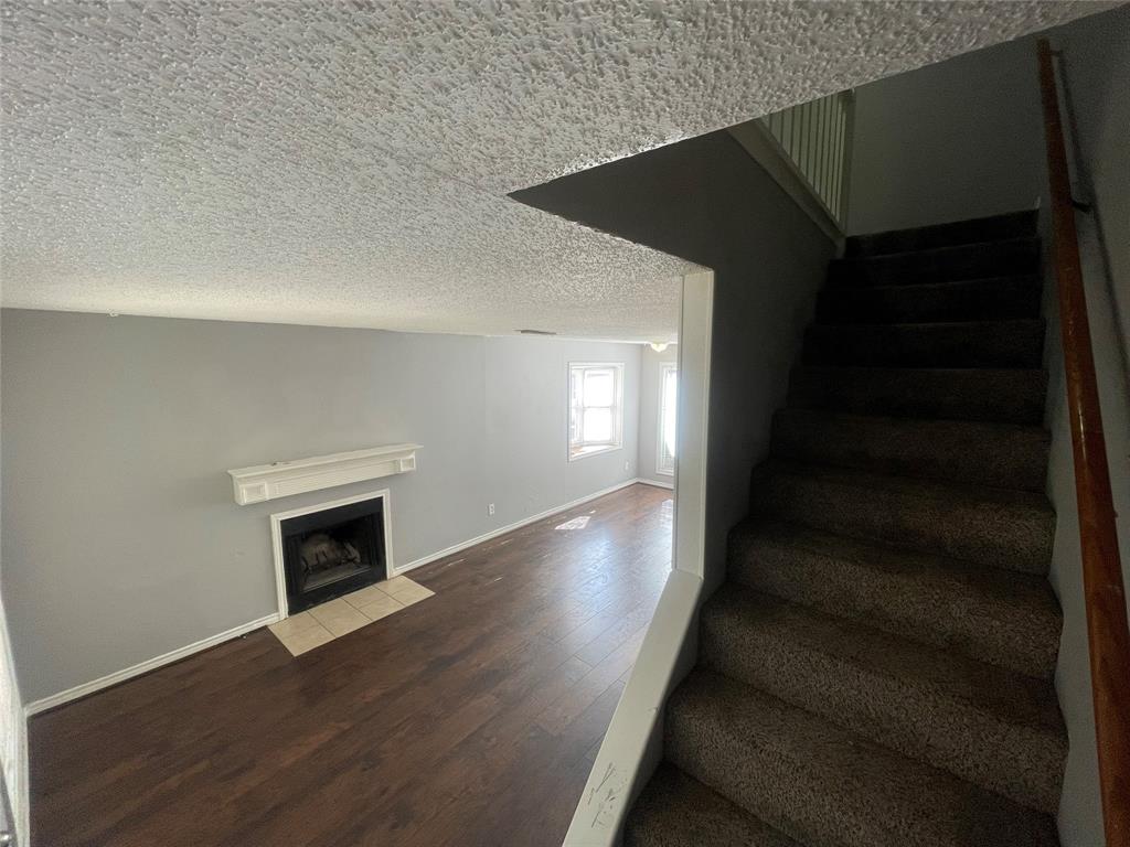 Wood-finish flooring, fireplace with a decorative mantel, neutral-toned walls, and a staircase with a wooden handrail