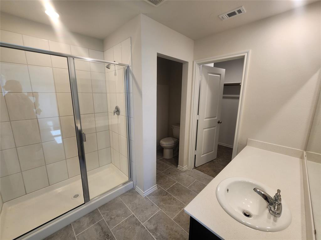 Tiled shower enclosure with sliding glass doors, single vanity with integrated sink and chrome faucet, and tiled flooring