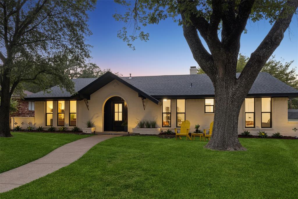 exterior with an arched entryway, dark trim windows, a paved walkway, and mature trees