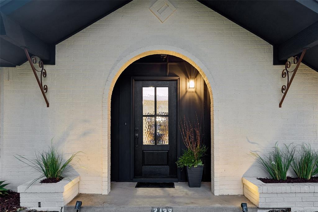 Arched entryway featuring a dark-paneled door with glass inserts, brick exterior, and decorative wrought iron brackets