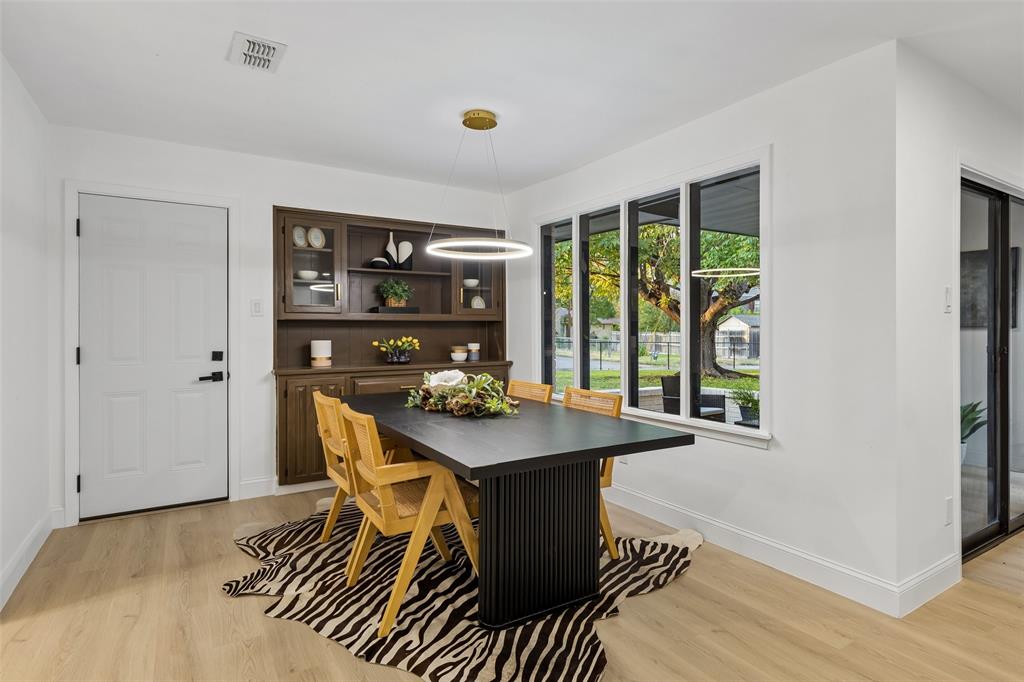 Light wood-finish flooring, built-in dark wood cabinetry with glass fronts, a contemporary linear chandelier, and multiple rectangular windows