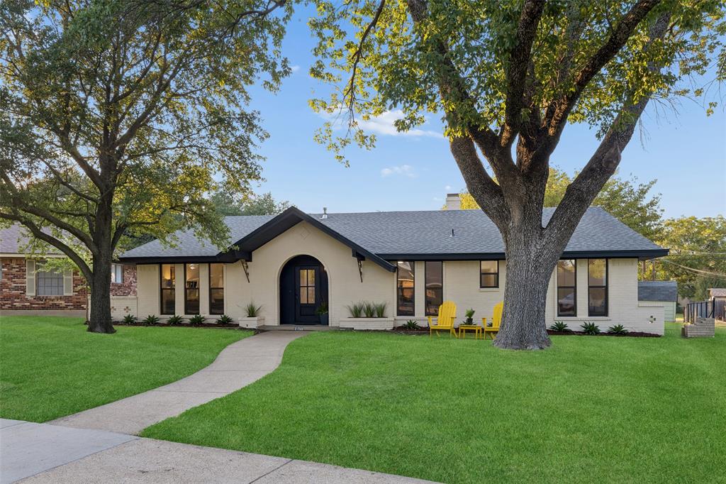 brick exterior with an arched entryway, dark trim windows, and a dark shingled roof