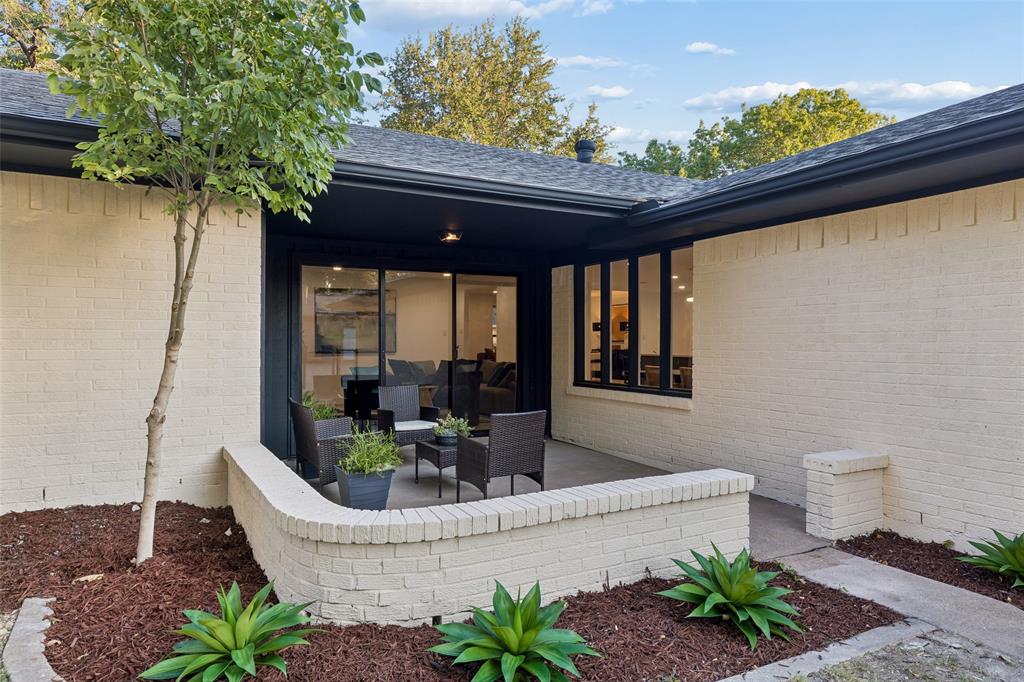 Brick exterior with dark trim accents, covered patio, large sliding glass doors, and a manicured landscape
