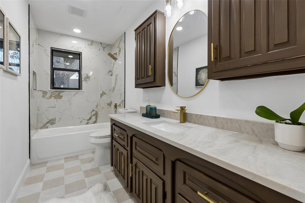 Spacious bathroom featuring a built-in bathtub with a tile surround, dark wood-finish cabinetry, a single vanity with an undermount sink, and a circular mirror