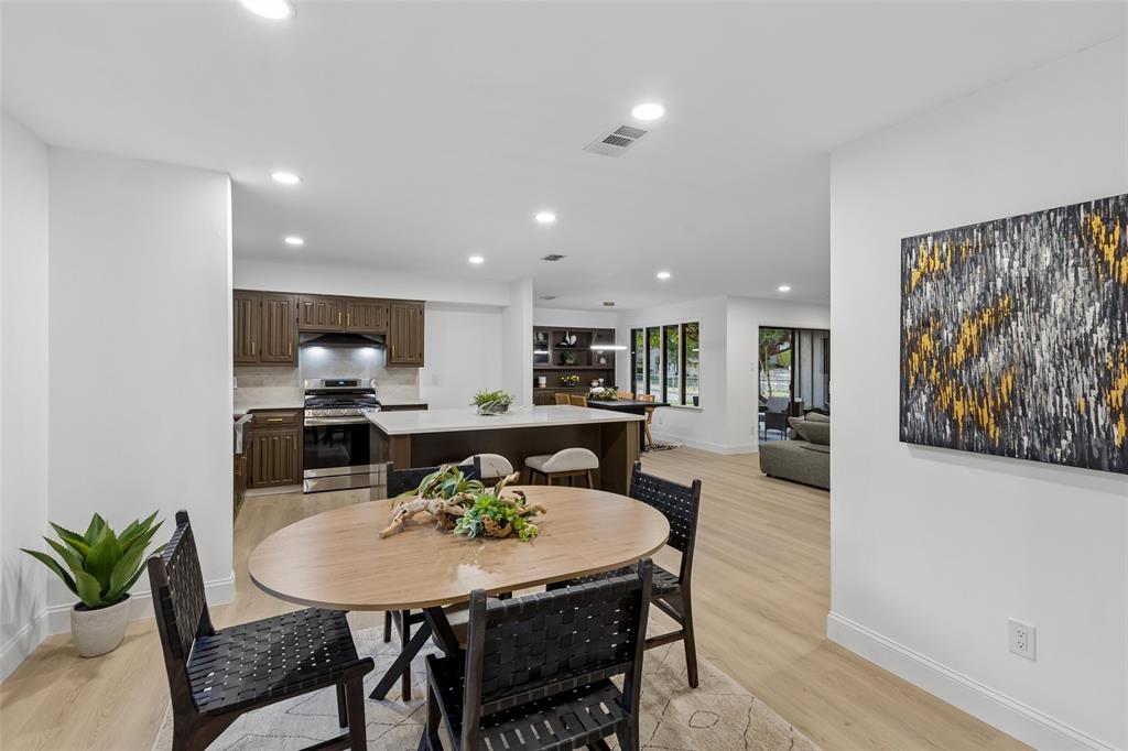 Open-concept interior featuring recessed lighting, light wood-finish flooring, a kitchen with dark wood cabinetry, a center island with counter seating, and stainless steel appliances