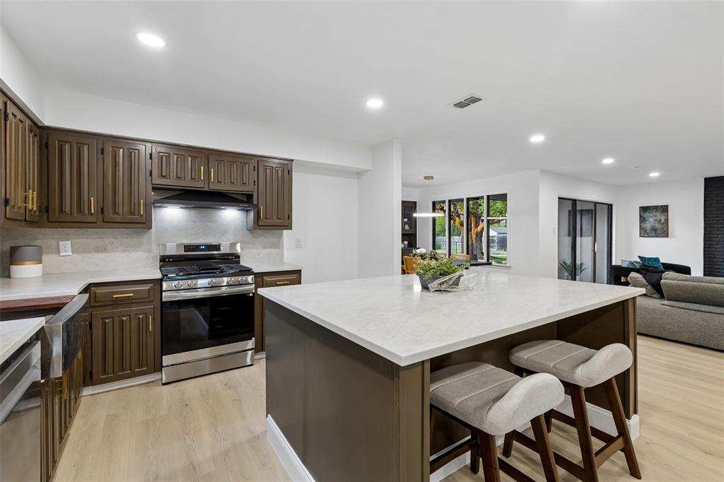 Modern kitchen featuring an expansive island with a light-toned countertop, stainless steel appliances, dark wood-finish cabinetry, and recessed lighting