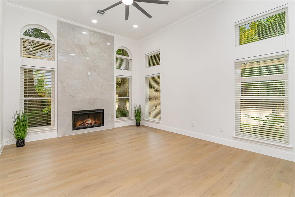 Unfurnished living room with ornamental molding, ceiling fan, a premium fireplace, a towering ceiling, and light wood-type flooring