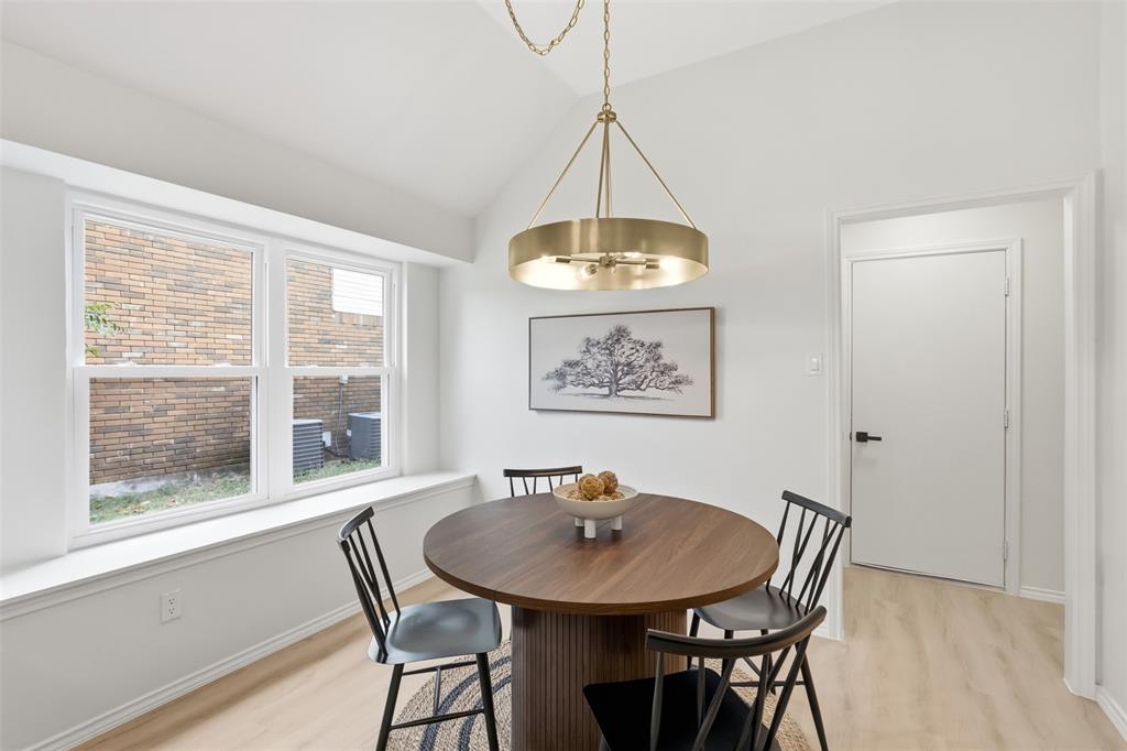 Vaulted ceiling, contemporary chandelier, light wood-finish flooring, white walls, and a large window with a deep sill