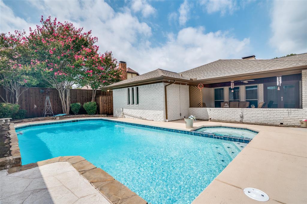 Swimming pool with integrated spa, concrete decking, wood fencing, and mature flowering trees