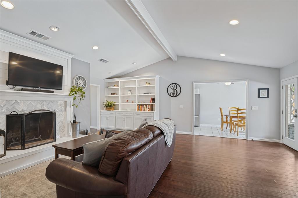 Vaulted ceiling with exposed beams, wood-finish flooring, built-in shelving, fireplace with decorative tile surround, and recessed lighting