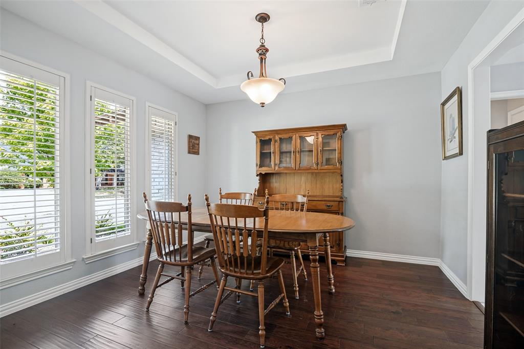 Hardwood-style flooring with white trim, a tray ceiling, and a prominent chandelier