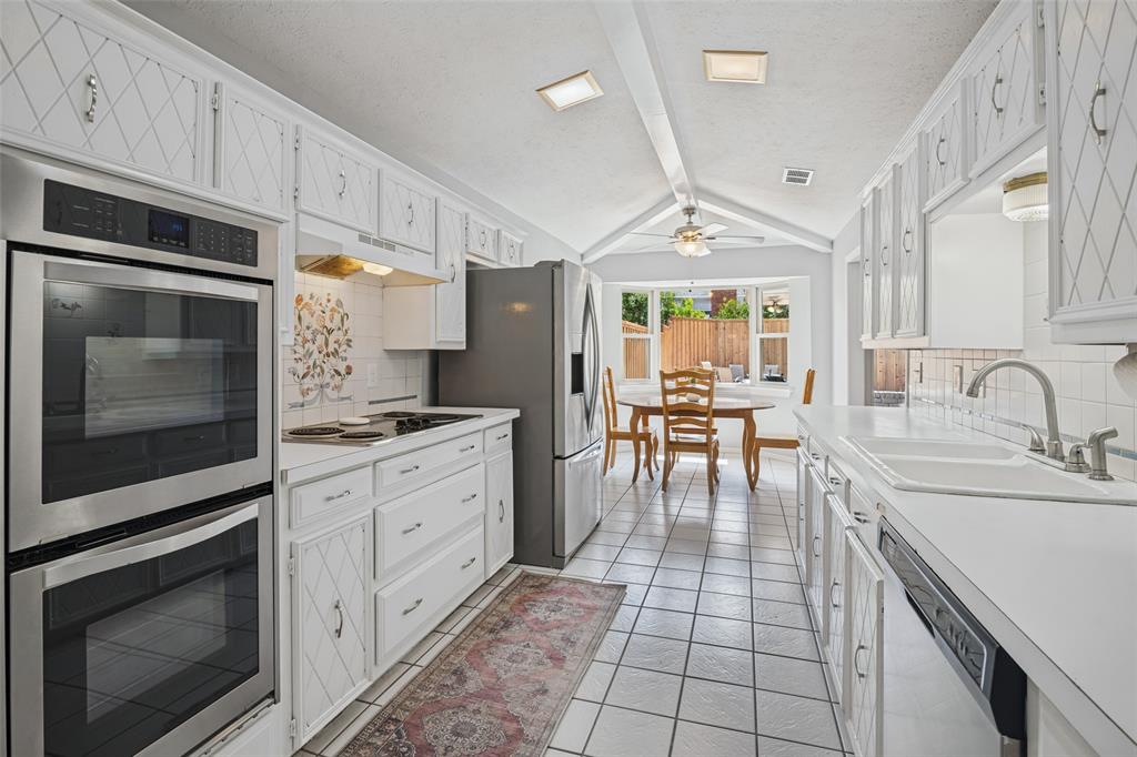 Galley kitchen featuring white cabinetry, tile flooring, stainless steel double ovens, and a built-in dishwasher