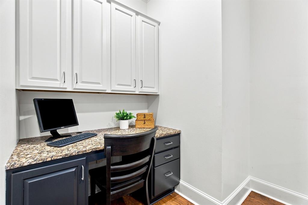 Built-in desk with a stone-finish countertop, white upper cabinetry, dark lower cabinetry, and wood-finish flooring off of the breakfast nook.