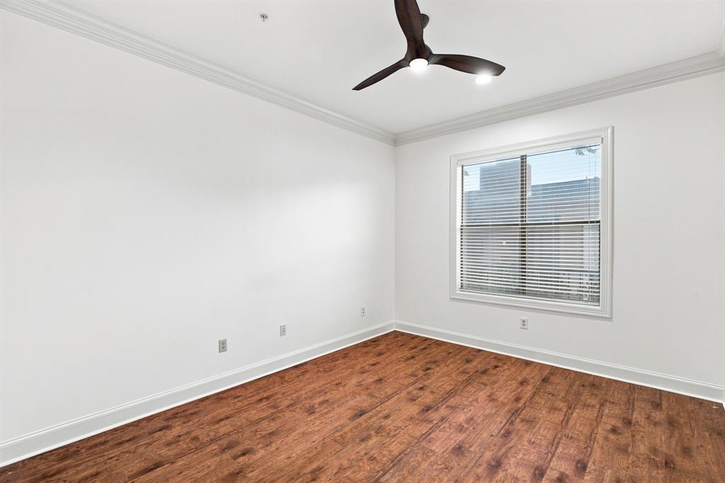 Guest bedroom with wood-finish flooring, white walls, crown molding, a window with blinds, and a dark-toned ceiling fan with integrated lighting