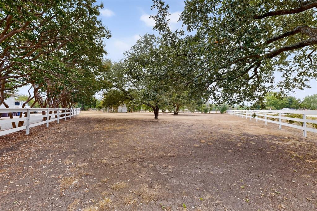 Expansive open lot featuring mature trees and white fencing
