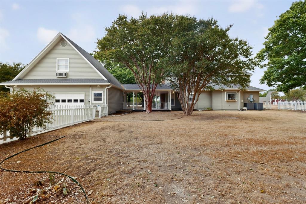Exterior siding with an attached garage, featuring a white picket fence, a covered walkway, and mature trees