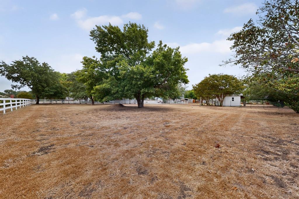 Expansive open land with mature trees and a white post-and-rail fence