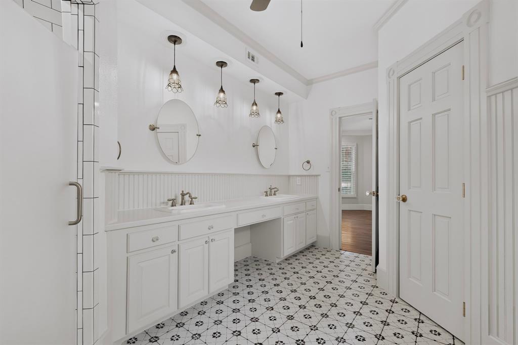 Spacious bathroom featuring a dual vanity with white cabinetry, patterned floor tiling, and a shower enclosure with subway tile