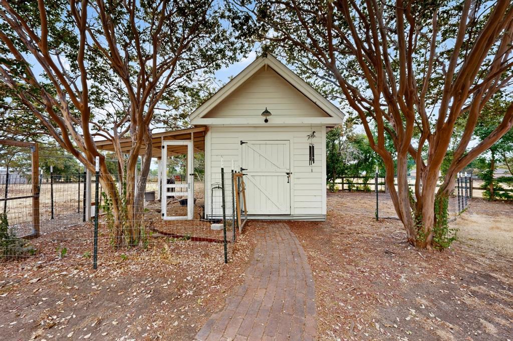 White wood-paneled outbuilding with a gable roof, barn-style door, and attached covered extension