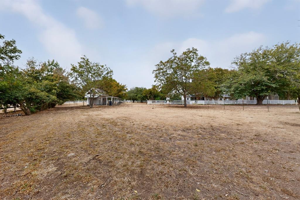 Expansive outdoor area with a white picket fence, mature trees, and a visible outbuilding